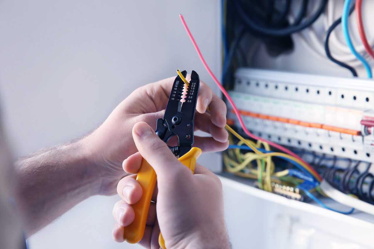 Electrician stripping a cable beside an open consumer unit